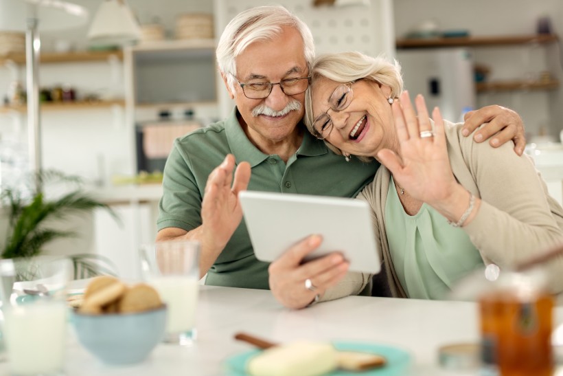 elderly couple smiling at their loved ones and waving through video chat