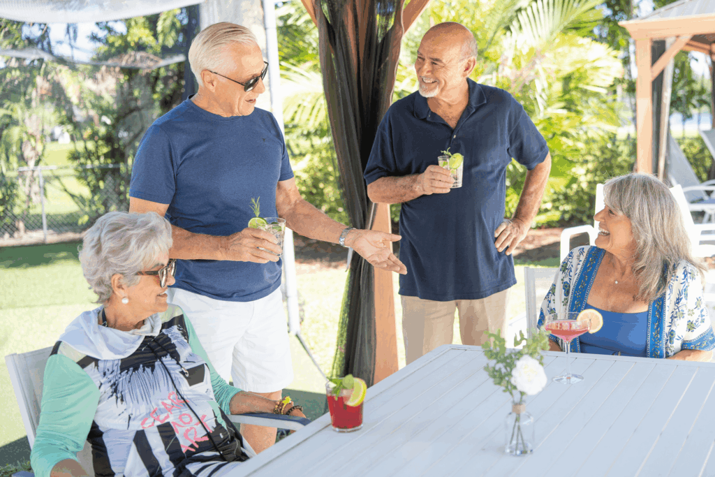 Four older adults enjoy drinks and conversation outdoors on sunny day.