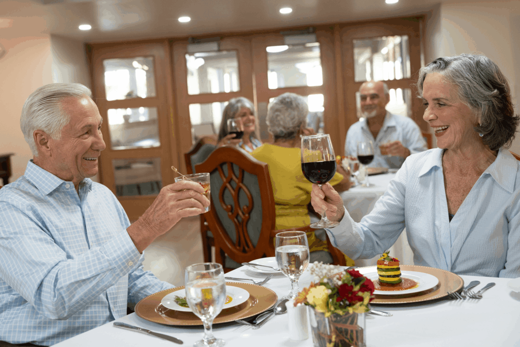 A cheerful couple toasts at an elegant dining table with others enjoying wine and meals nearby.