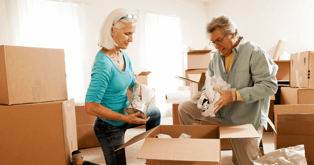 Two people unpacking boxes with items inside in a bright room.