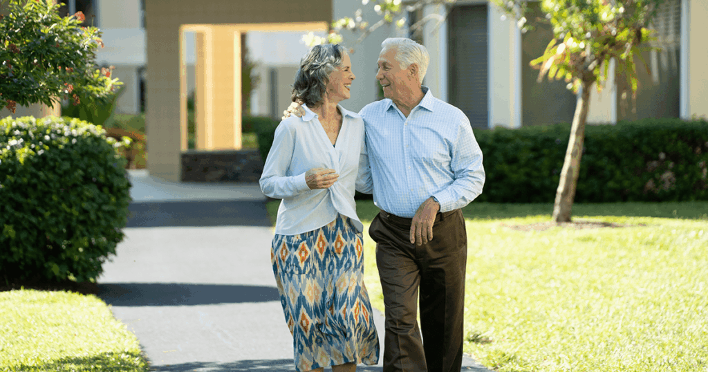 A happy couple walks arm-in-arm on a sunny day near their home.