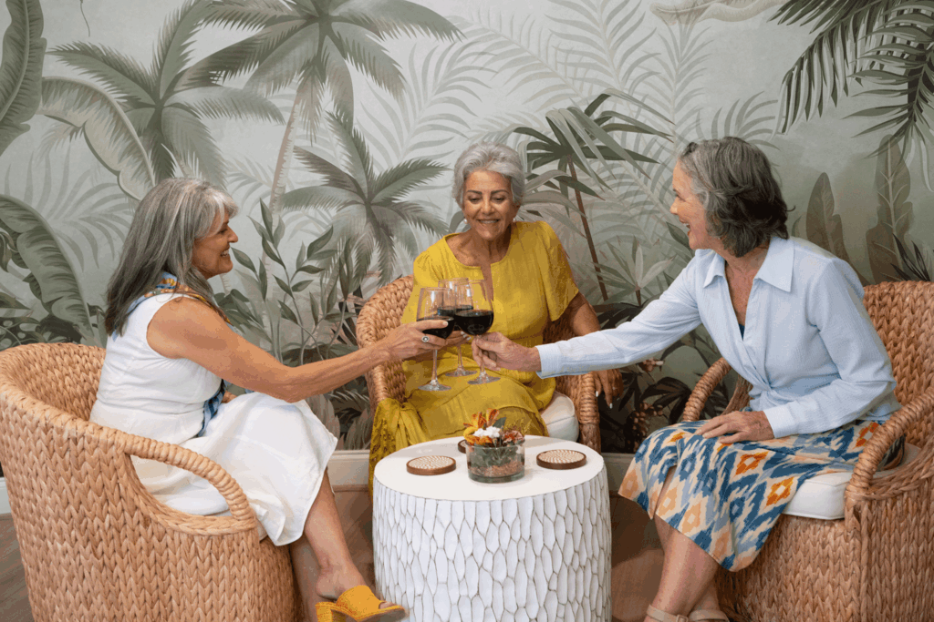 Three women toast with wine glasses at a tropical-themed setting.