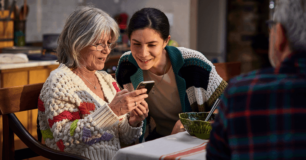 Two women share a moment with a smartphone at a table indoors.