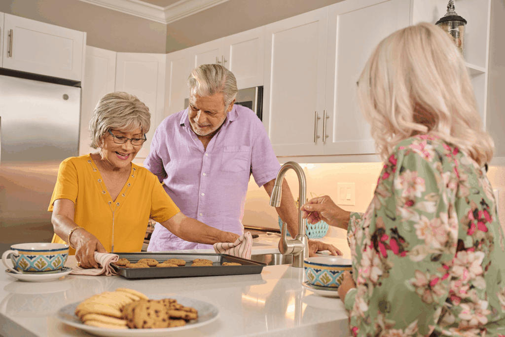 Three people share kitchen joy over freshly baked cookies and tea.