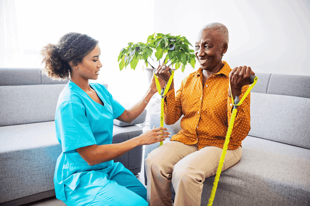 Nurse assists elderly woman with resistance band exercise on couch.