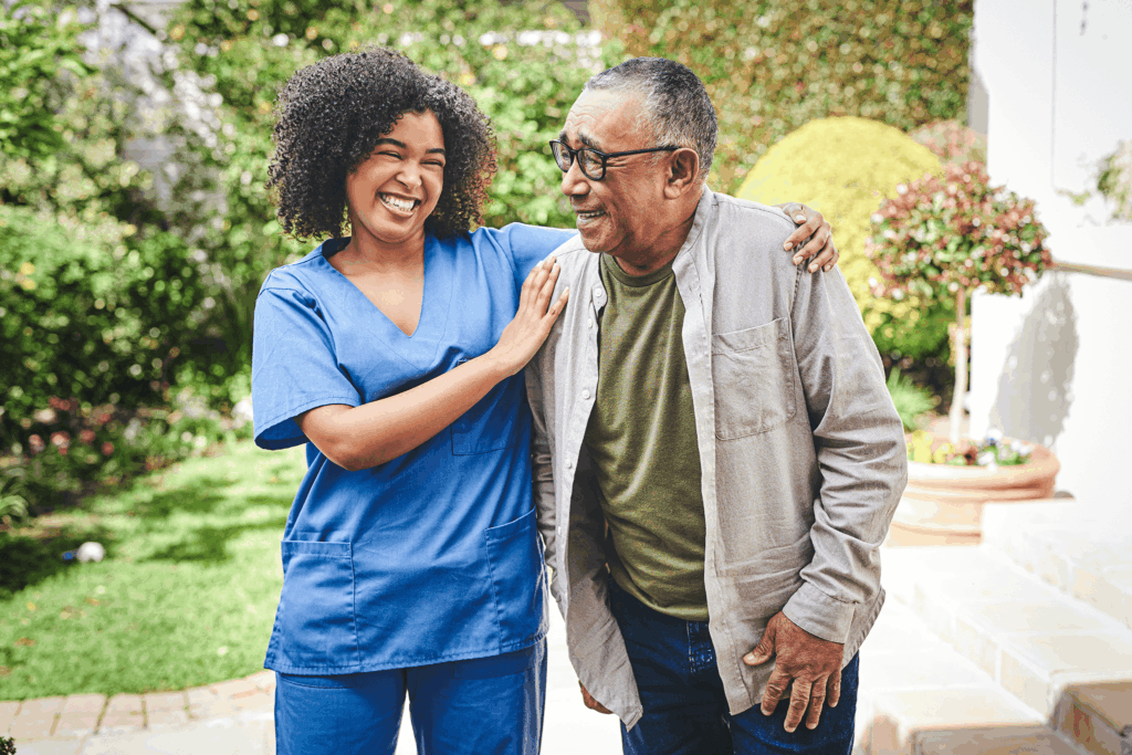 A caregiver and senior share a joyful moment outdoors near greenery.