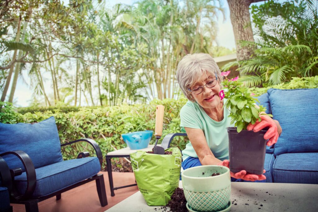 Woman gardening outdoors with potted plants and soil on patio table.