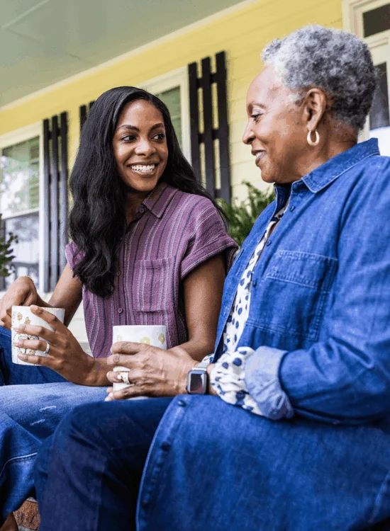 Two women share smiles and tea on porch steps.