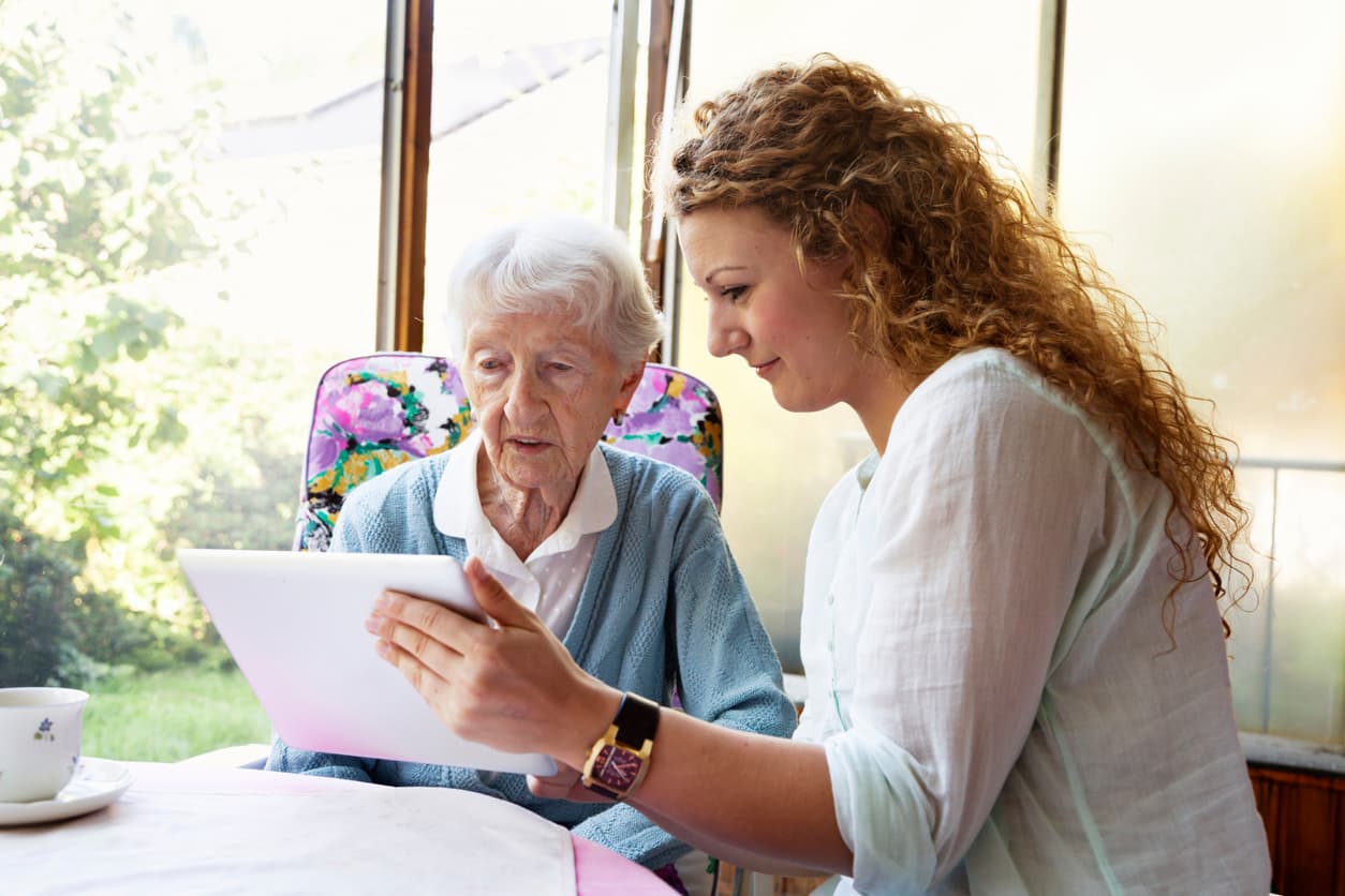Young caregiver showing something to senior woman on digital tablet.