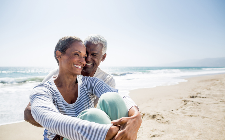 senior husband and wife sitting on the beach