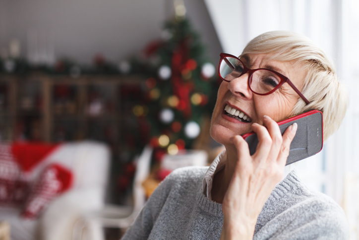 Older woman on the phone with Christmas decorations in backdrop.