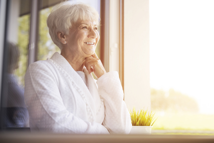 Older adult woman smiling while looking out a window.