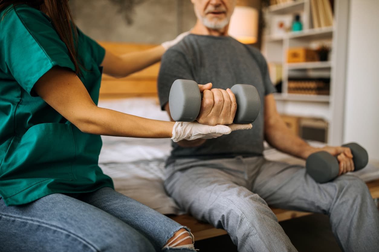 Older man working with a weight with assistance from therapist.